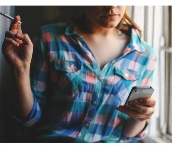 Woman with multicolored shirt smoking a cigarette while scrolling on phone 