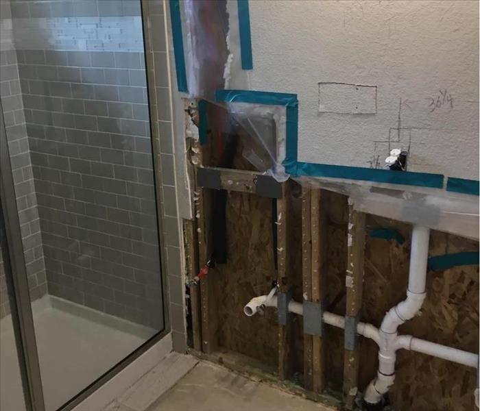 A bathroom with the bottom of the walls removed, exposing pipes and wall studs