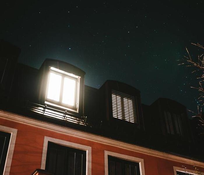 Exterior of a house at night with a single window lit