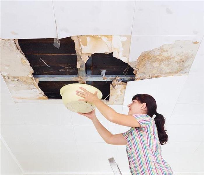 Woman with black hair and rainbow shirt holding a bowl under large hold in ceiling