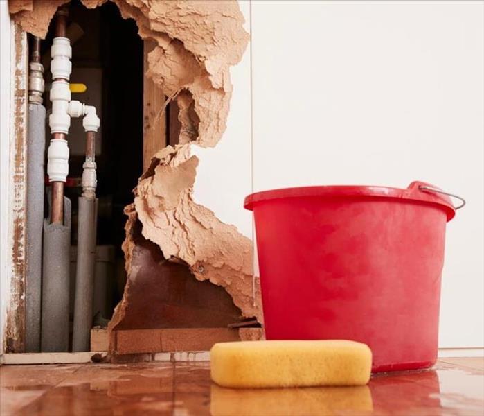 Red bucket and sponge sitting in a pool of water with large hole in wall in background